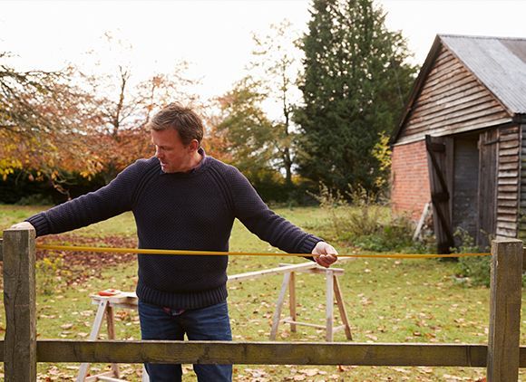 a man is measuring a wooden fence with a tape measure .