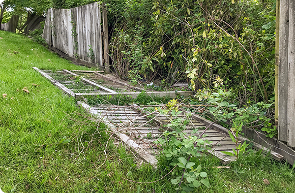 a fallen piece of fence is sitting in the grass next to a wooden fence .