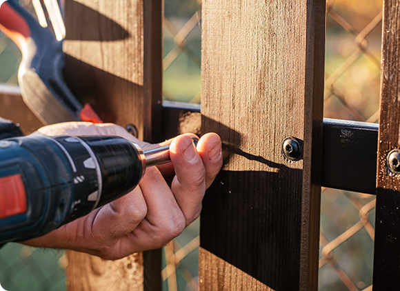 a man is using a drill to fix a wooden fence .