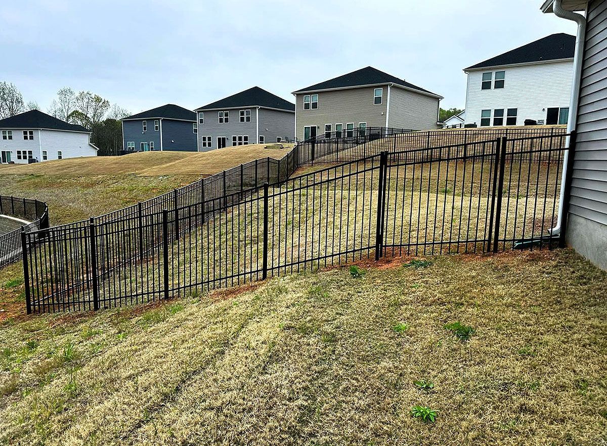 Black metal fence along sloped grass in a suburban backyard with houses in the background