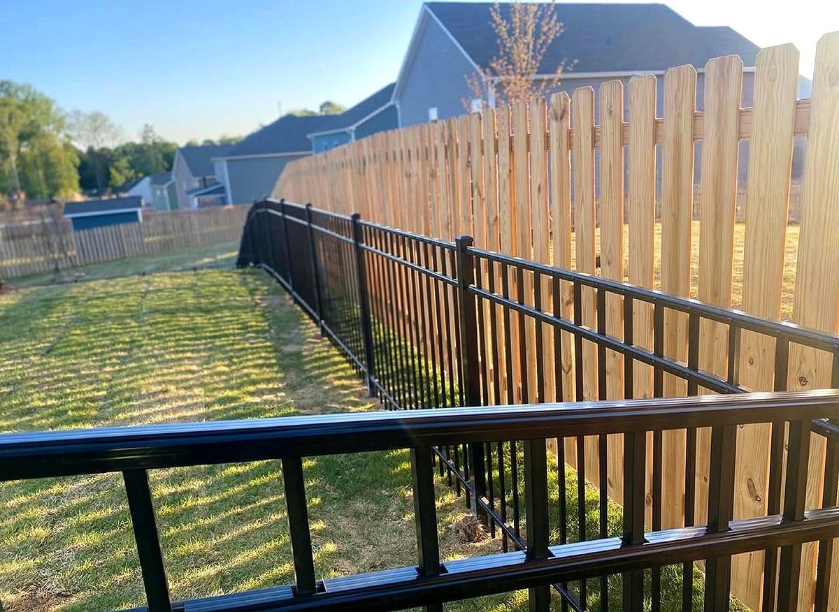 Backyard with black metal fence beside a tall wooden privacy fence in sunlight