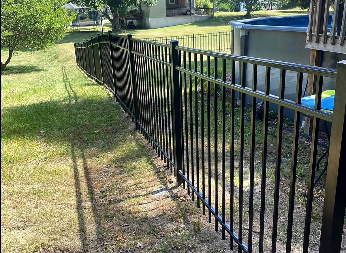 Black metal fence along a grassy yard beside a pool and house in bright daylight