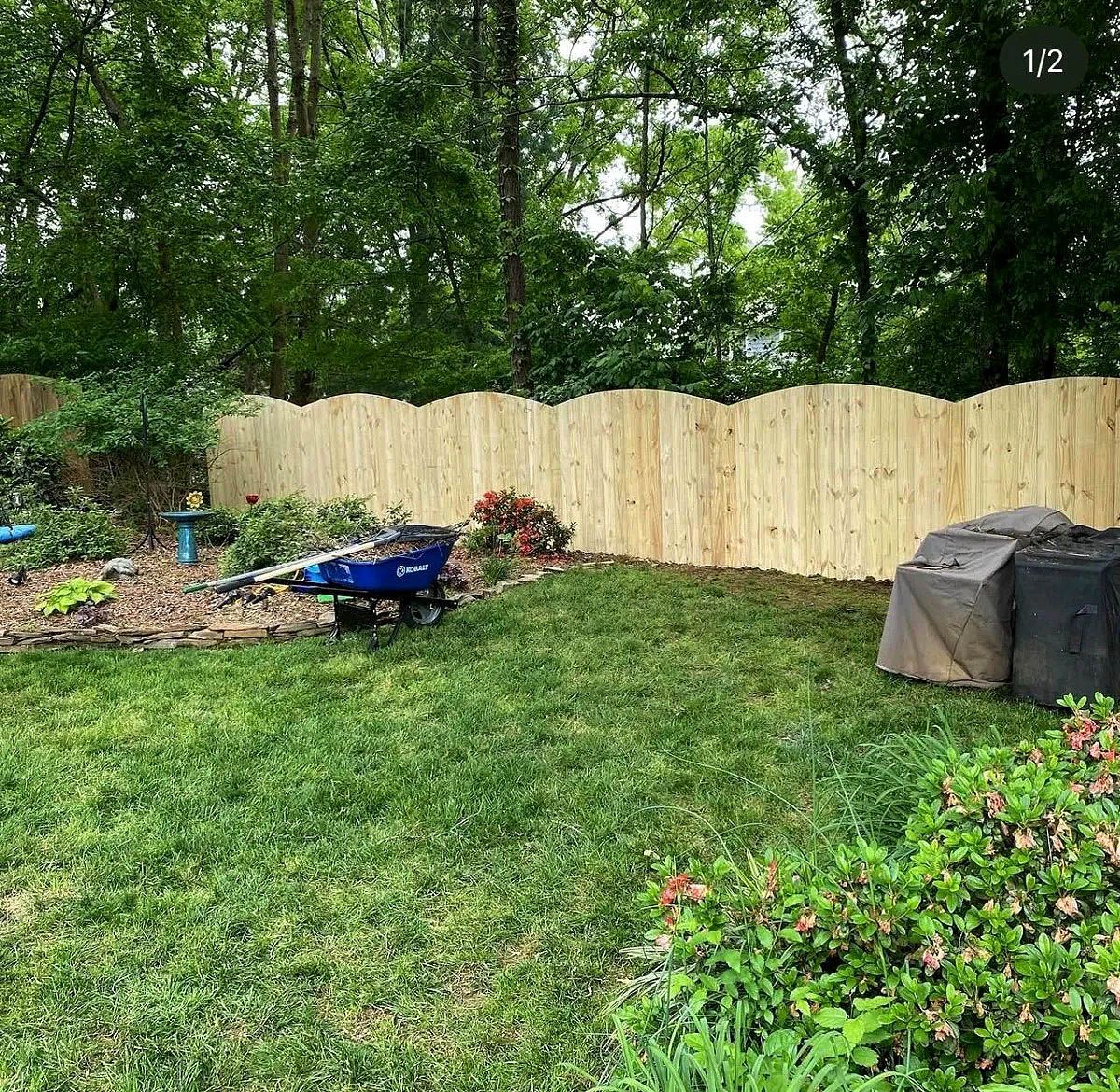 Backyard with new wooden fence, green lawn, trees, flower beds, and a covered grill