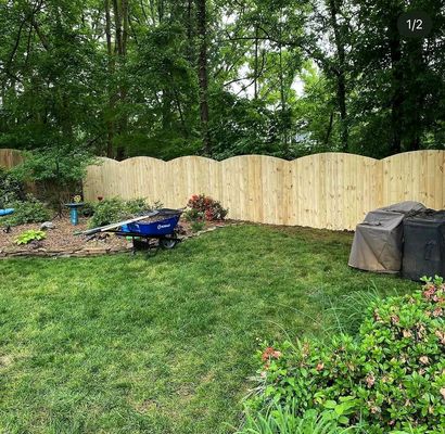 Backyard with fresh grass, new wooden fence, trees, and a blue wheelbarrow near a covered grill
