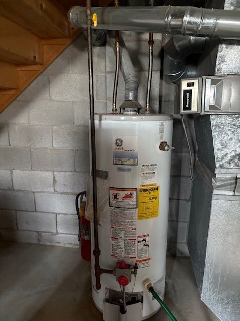 Technician repairing combi Gas Boiler Serenity Home Services LLC - A white water heater is sitting in a basement next to a staircase.