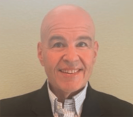 A bald man in a suit and tie is smiling for the camera.