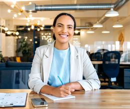 A woman is sitting at a desk in an office smiling at the camera.