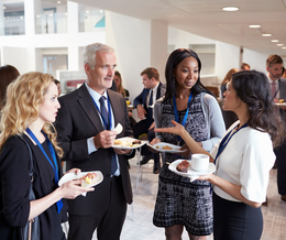 A group of people are standing around talking and eating food.