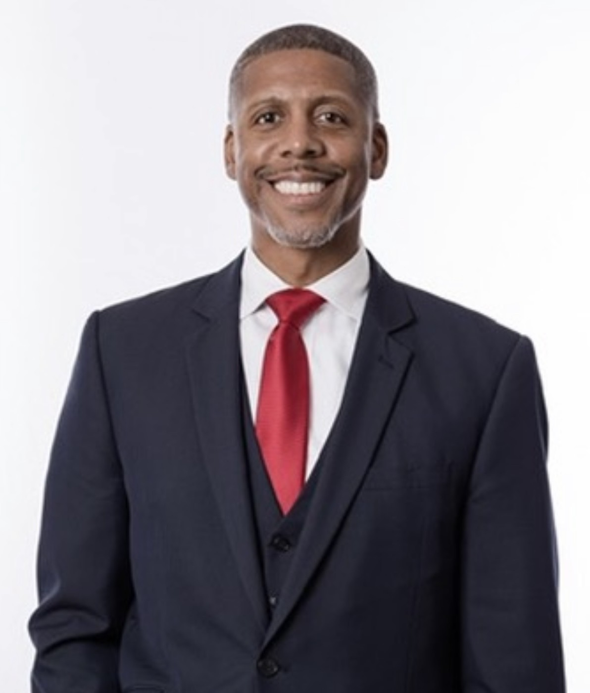 A man in a suit is sitting at a table with his hands folded.