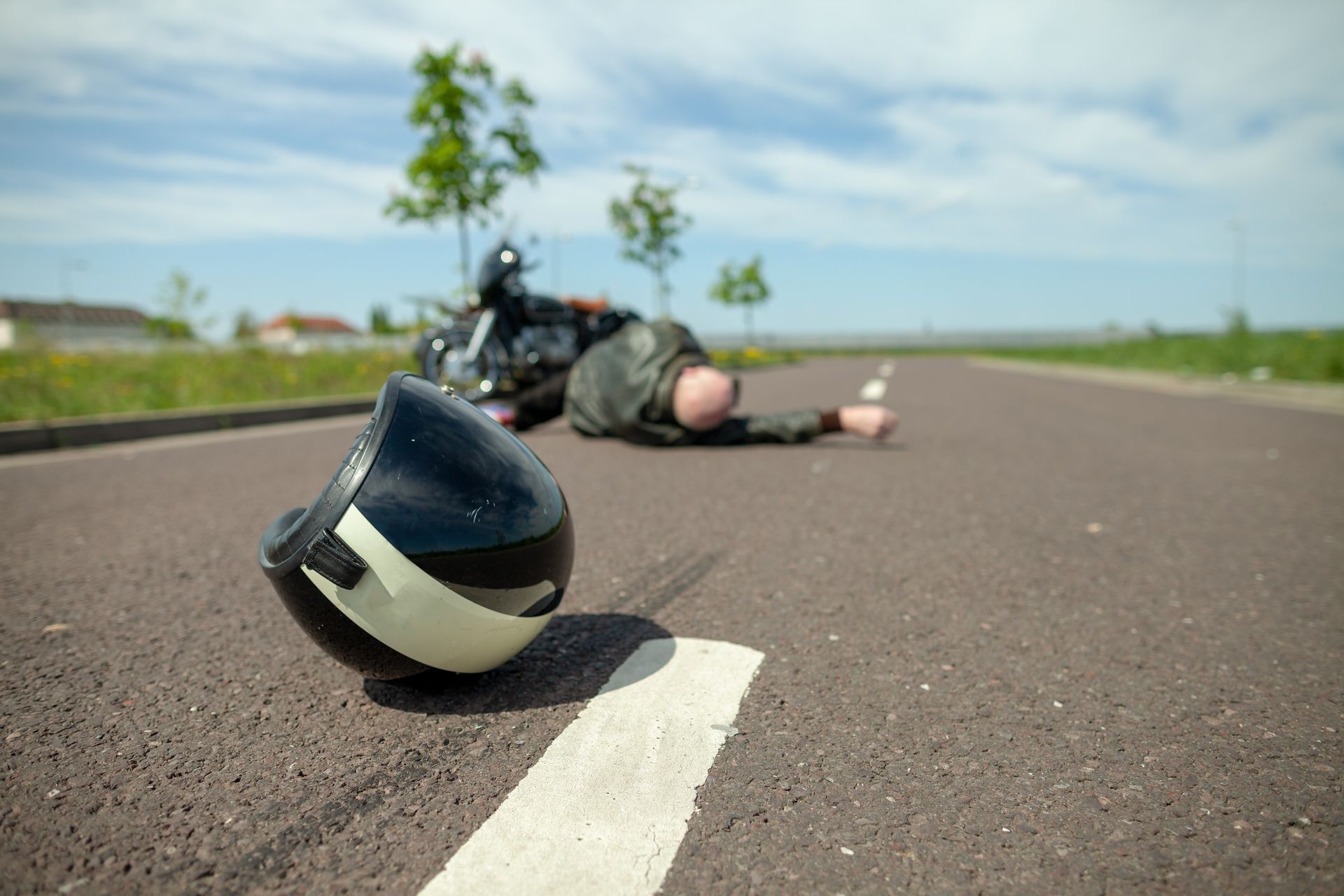 A man is laying on the side of the road next to a helmet.