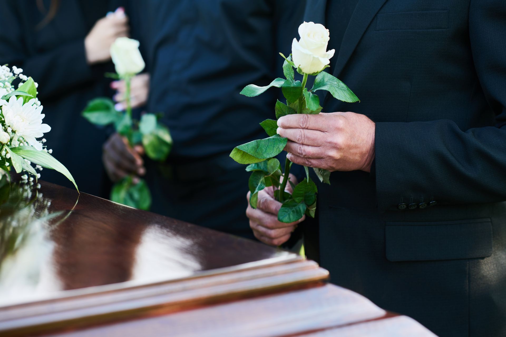 People holding white roses near a closed casket at a funeral.