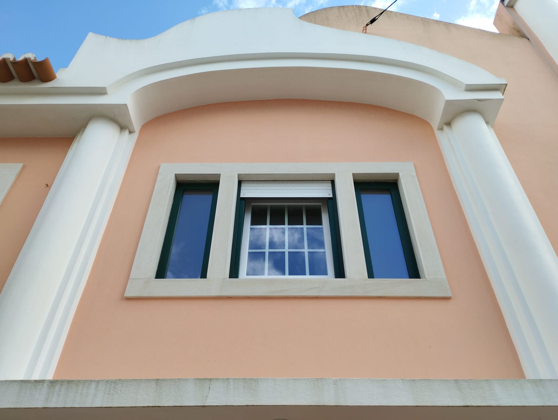 Janela em caixilharia de PVC branco com quadricula instalada em parede exterior com vista para jardim.