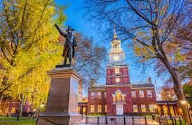 Statue of a man in front of Independence Hall, Philadelphia. Autumn foliage, blue sky.