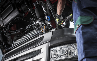 Mechanic working on the engine of a truck; wearing gloves and a blue uniform.