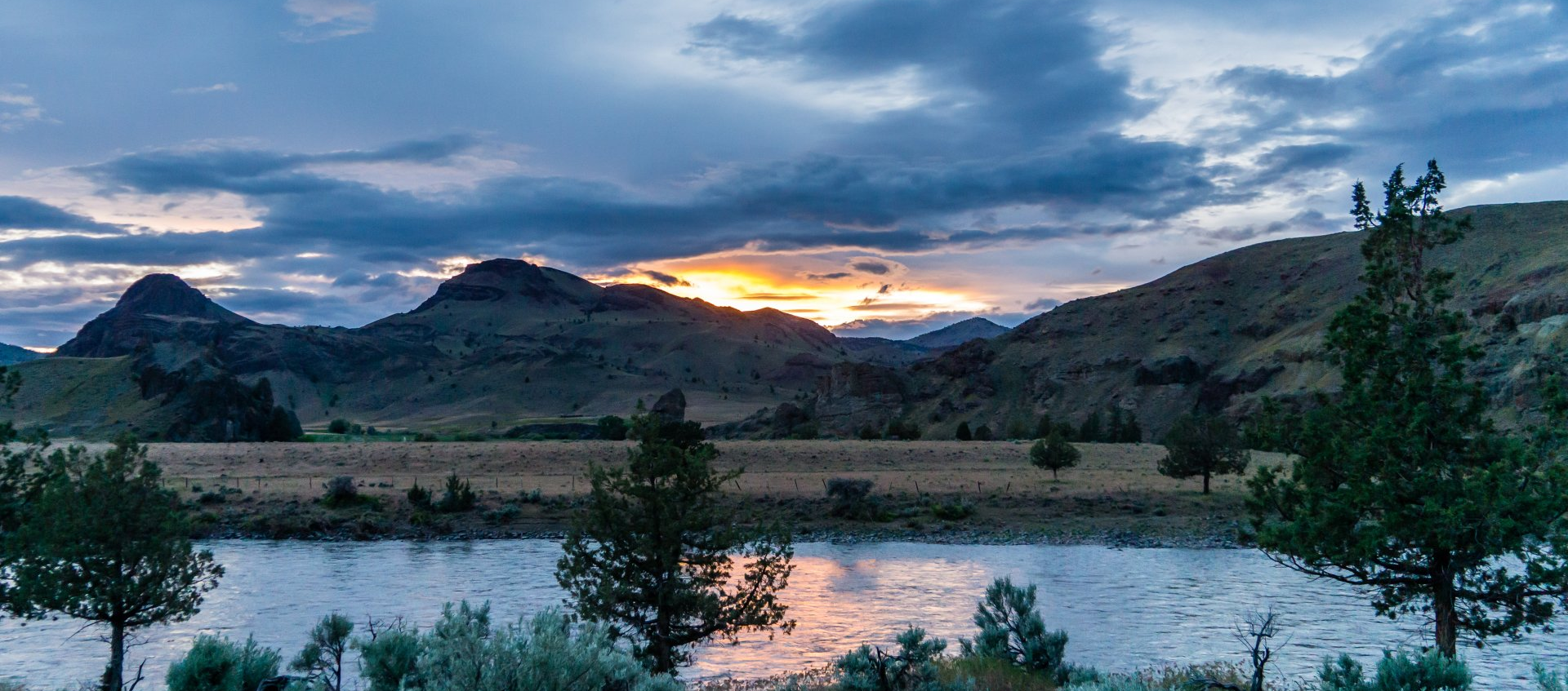 a sunset over a river with mountains in the background