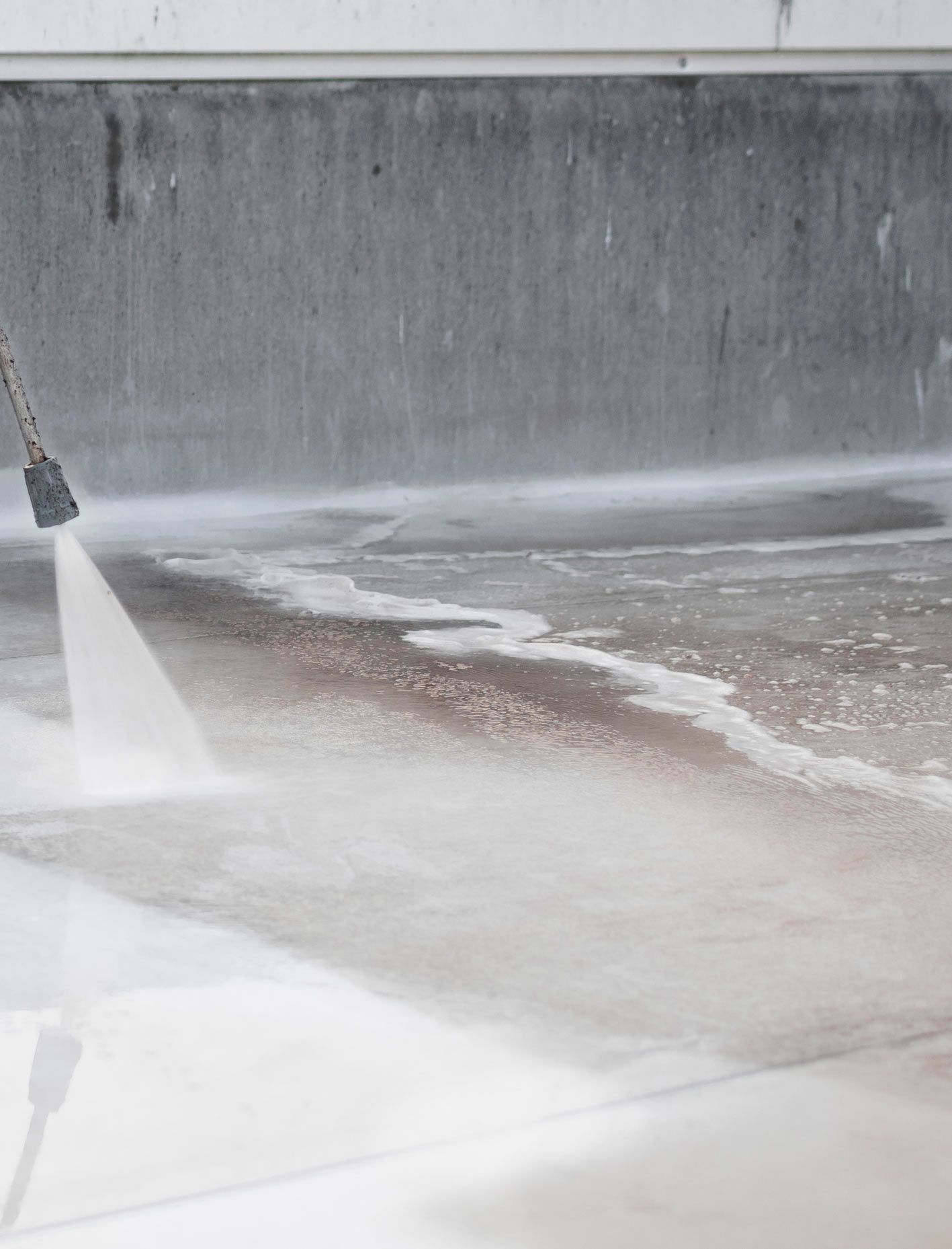 A Person is Using a High Pressure Washer to Clean a Concrete Floor — RPS–Remote Painting Services in White Rock, QLD