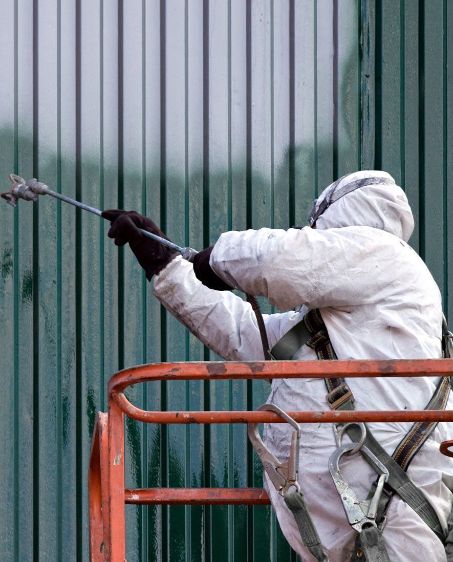 A Man in a Protective Suit is Spray Painting a Green Wall — RPS–Remote Painting Services in White Rock, QLD