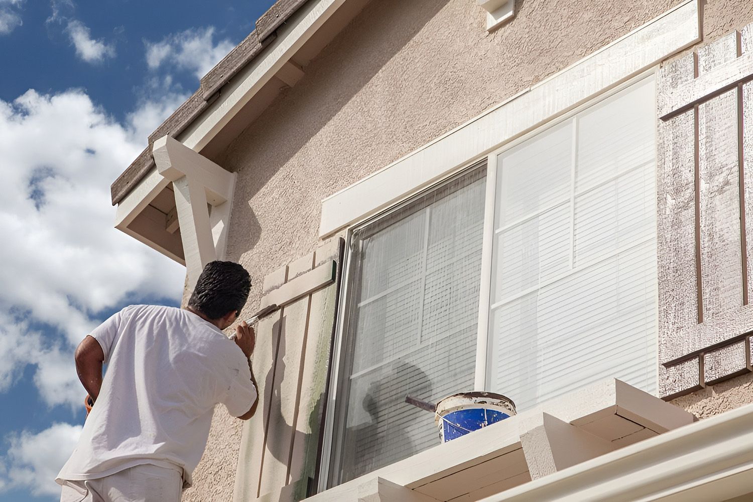 Person Painting Window Trim On A Beige Stucco House