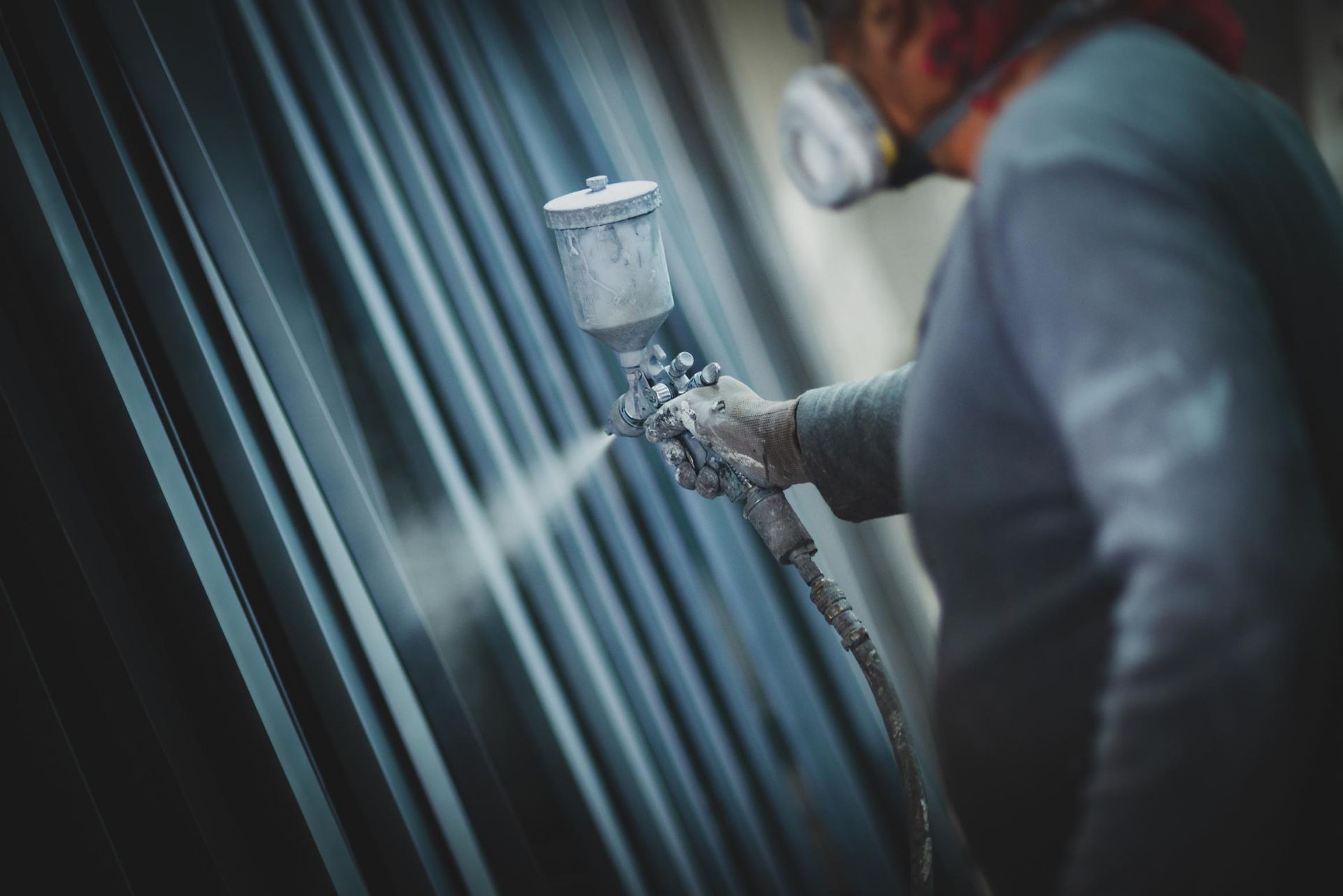 A Man Wearing a Mask is Spray Painting a Metal Wall — RPS–Remote Painting Services in Mareeba, QLD