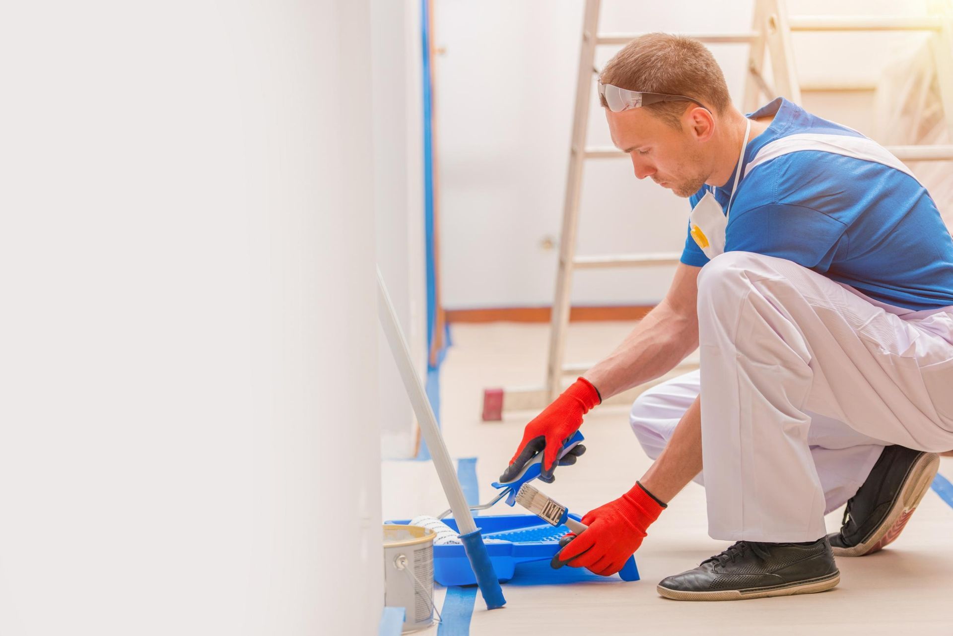 A Man is Kneeling Down While Painting a Wall — RPS–Remote Painting Services in Atherton, QLD