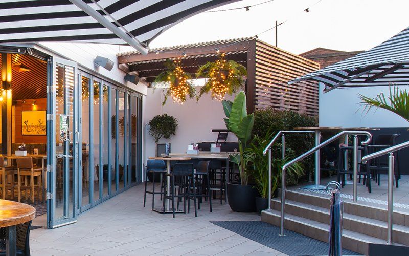 A restaurant with tables , chairs , umbrellas and stairs.