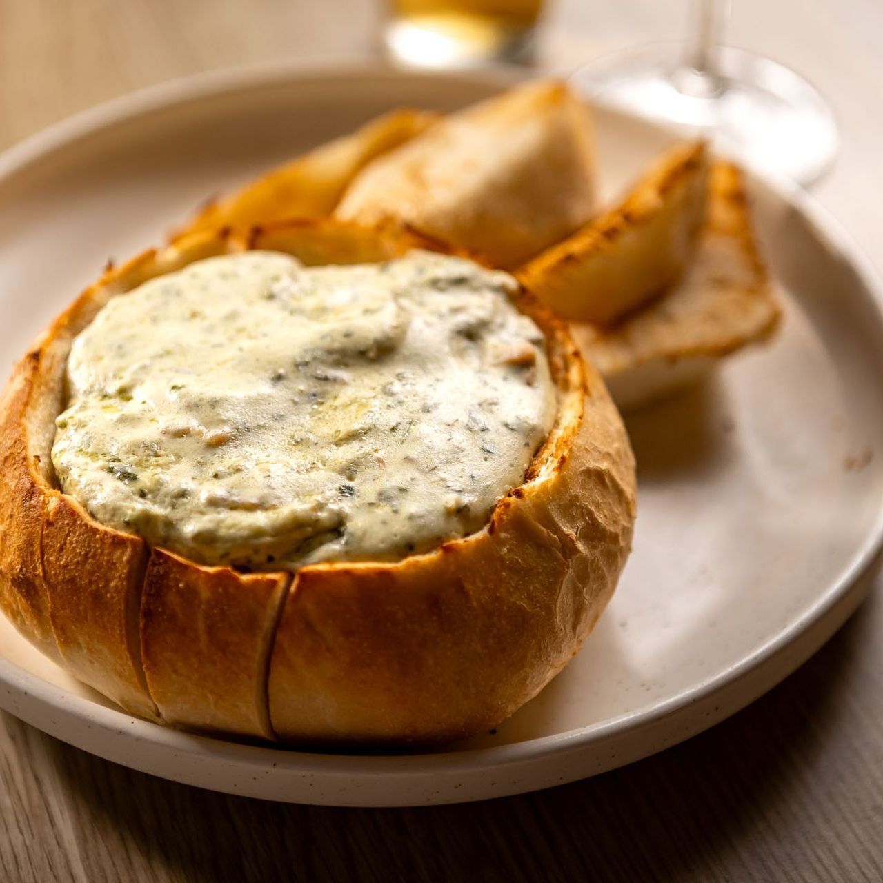 Spinach and artichoke dip served in a bread bowl with toasted bread wedges on a white plate.