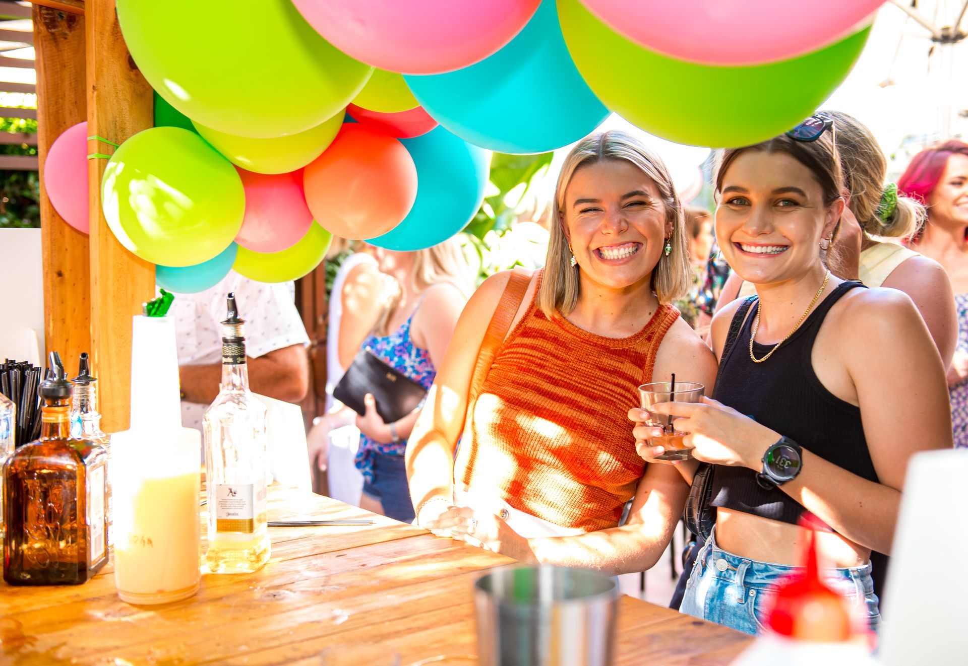 Two women are standing at a bar with balloons hanging from the ceiling.