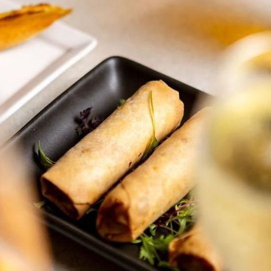 Spring rolls on a black plate with some green garnish.