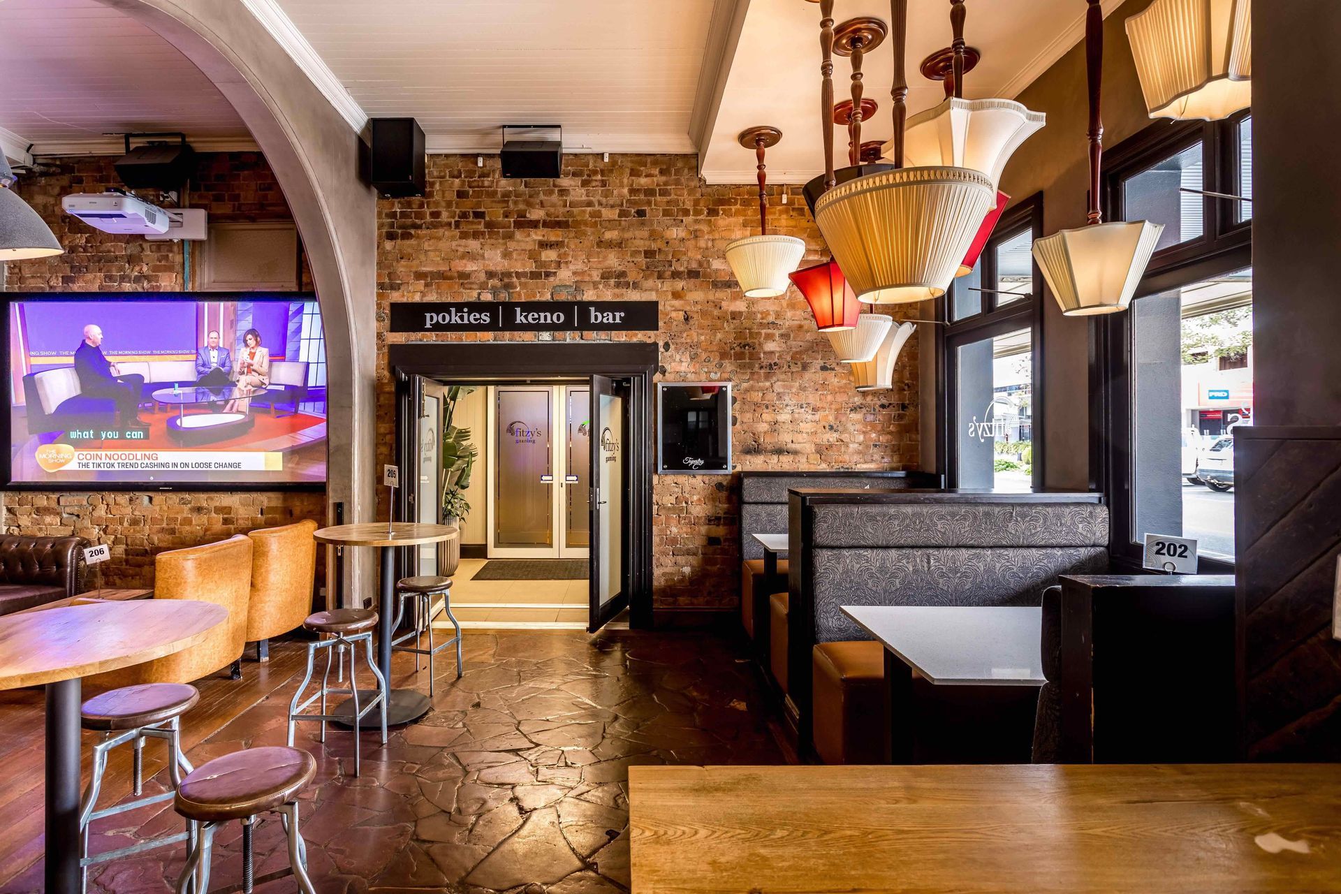 A restaurant with tables and chairs and a large screen on the wall.