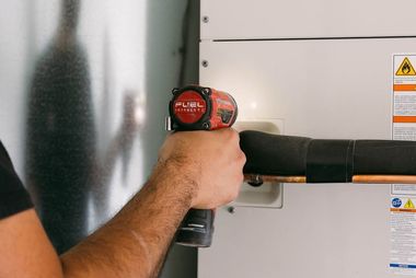Person using a red-and-black drill on a wall-mounted cabinet door