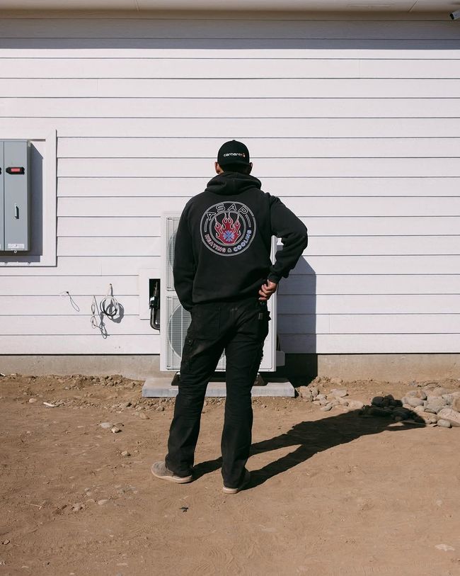 Person in black jacket stands facing a white garage door beside a house.