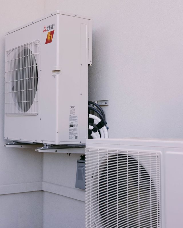 Two people standing by a wall-mounted boiler and plumbing setup indoors