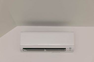 White wall-mounted air conditioner near the ceiling in a plain room