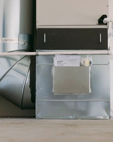 Metal HVAC ductwork with a taped insulation panel and vent opening in an indoor utility space
