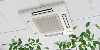 Ceiling-mounted white air conditioner above green plants in an office