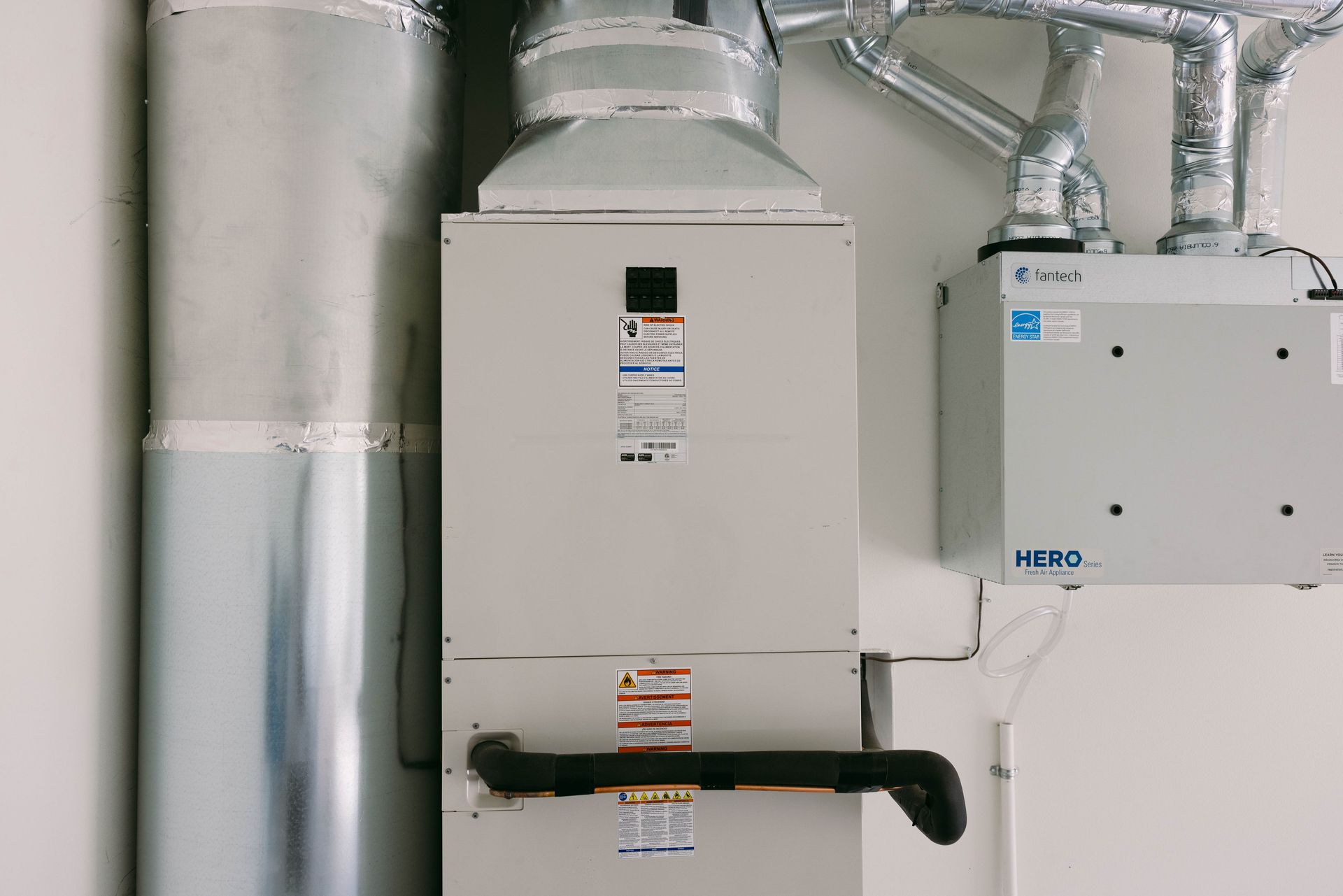 Basement HVAC equipment with silver ductwork and white control boxes on a wall