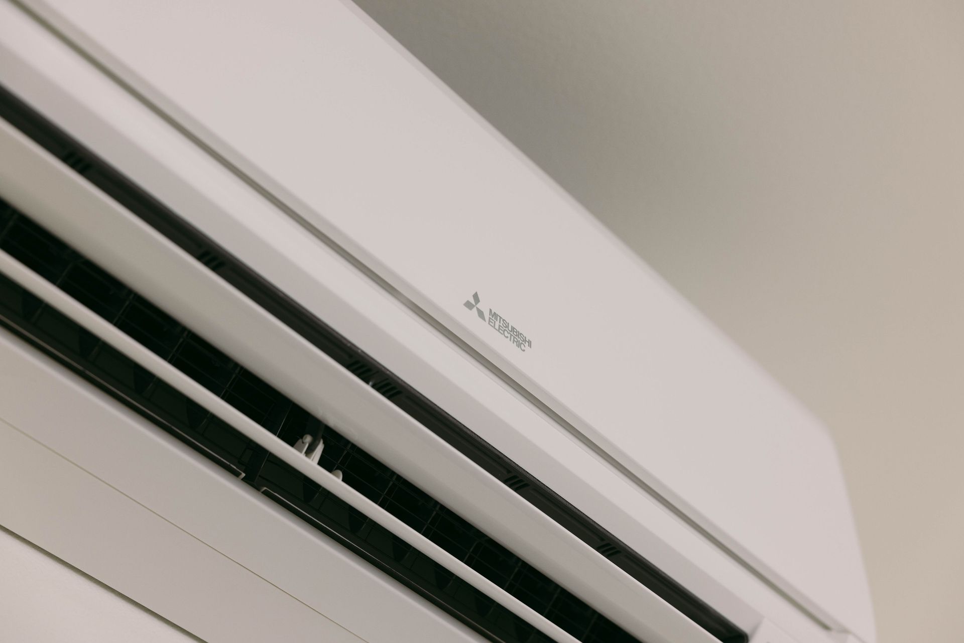 White wall-mounted air conditioner vent seen at an angle on a beige wall