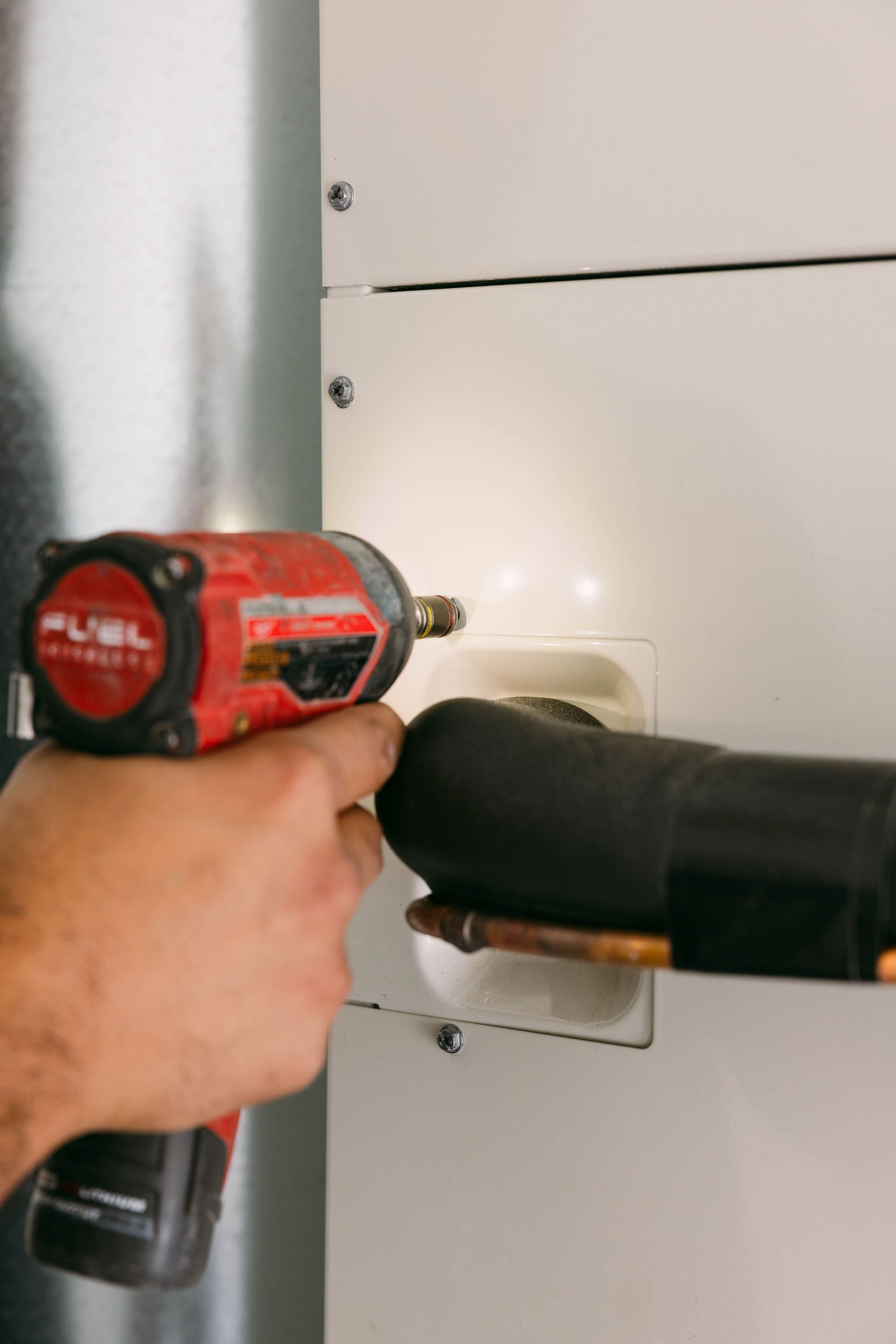 Person using a red cordless drill to install a black handle on a white cabinet door