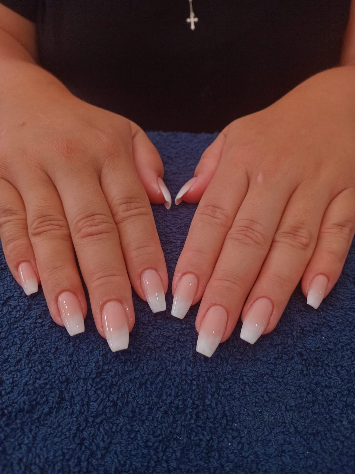 Hands displaying a fresh set of coffin-shaped French ombre acrylic nails against a blue background.