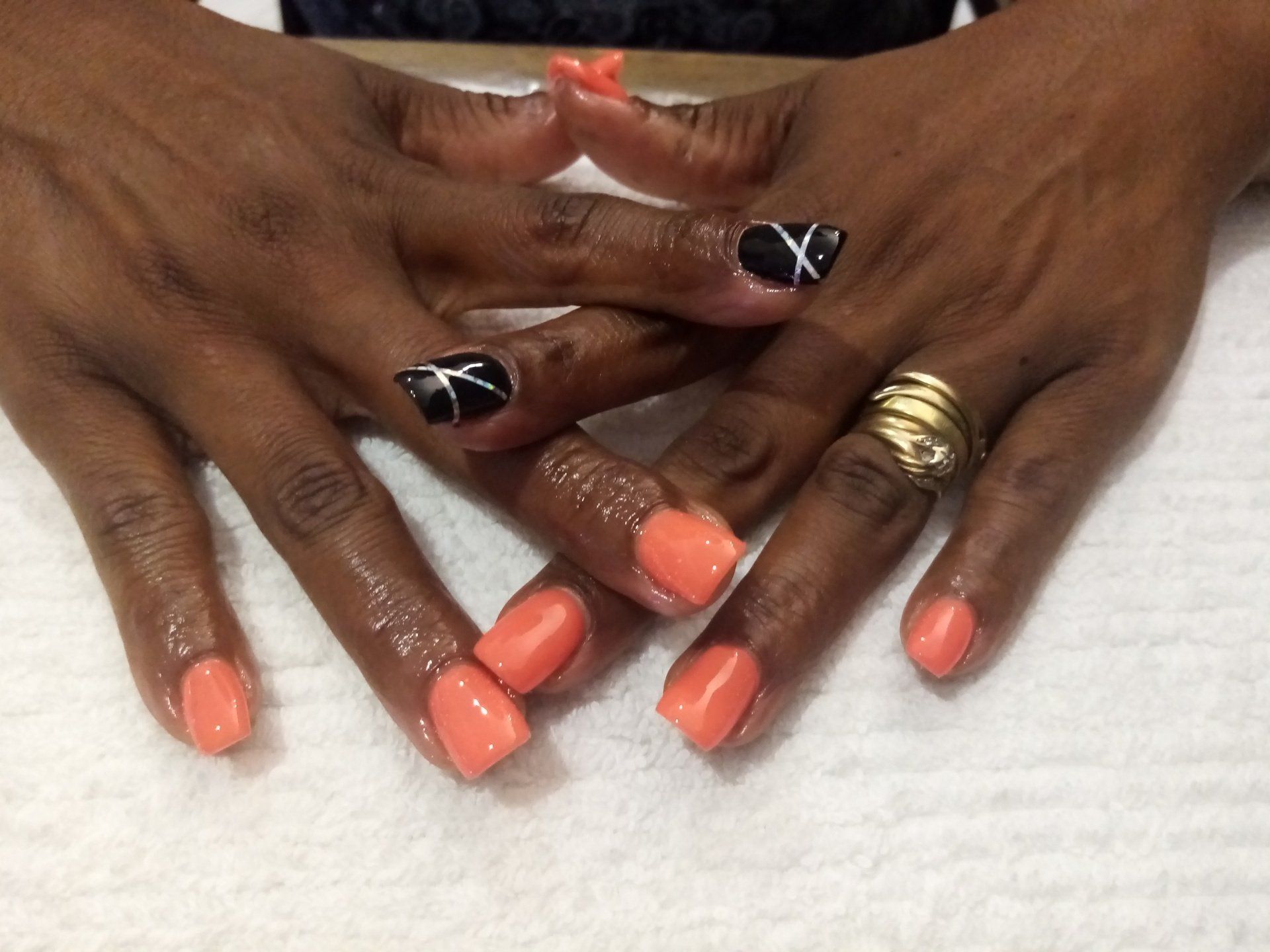 A woman 's hands with orange and black nails and a gold ring