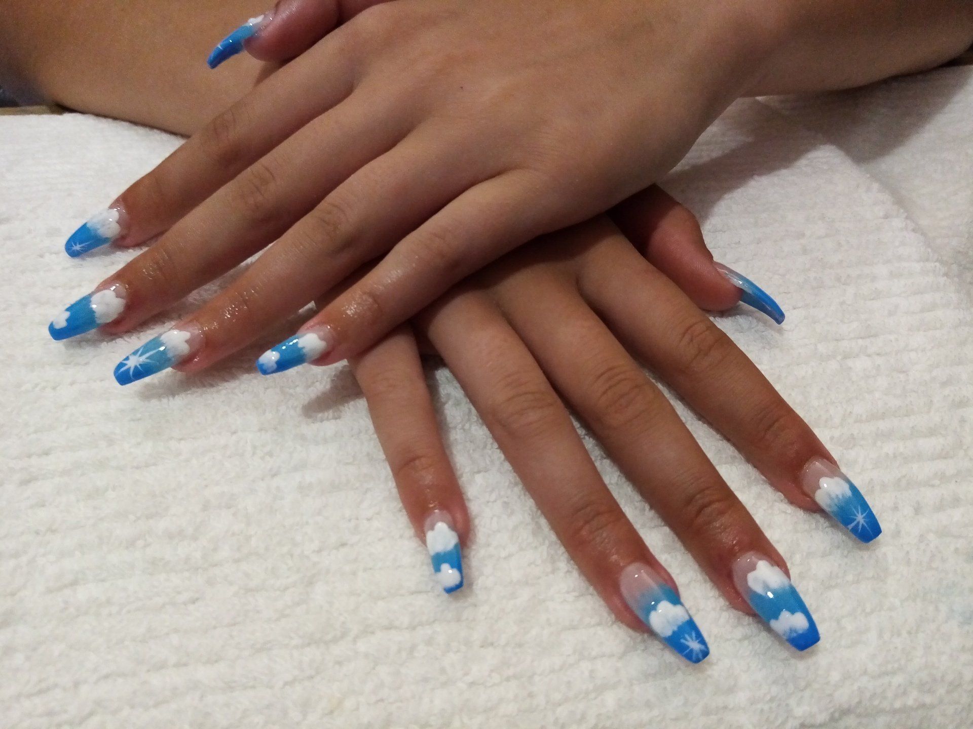 A woman 's nails are painted blue and white with clouds on them
