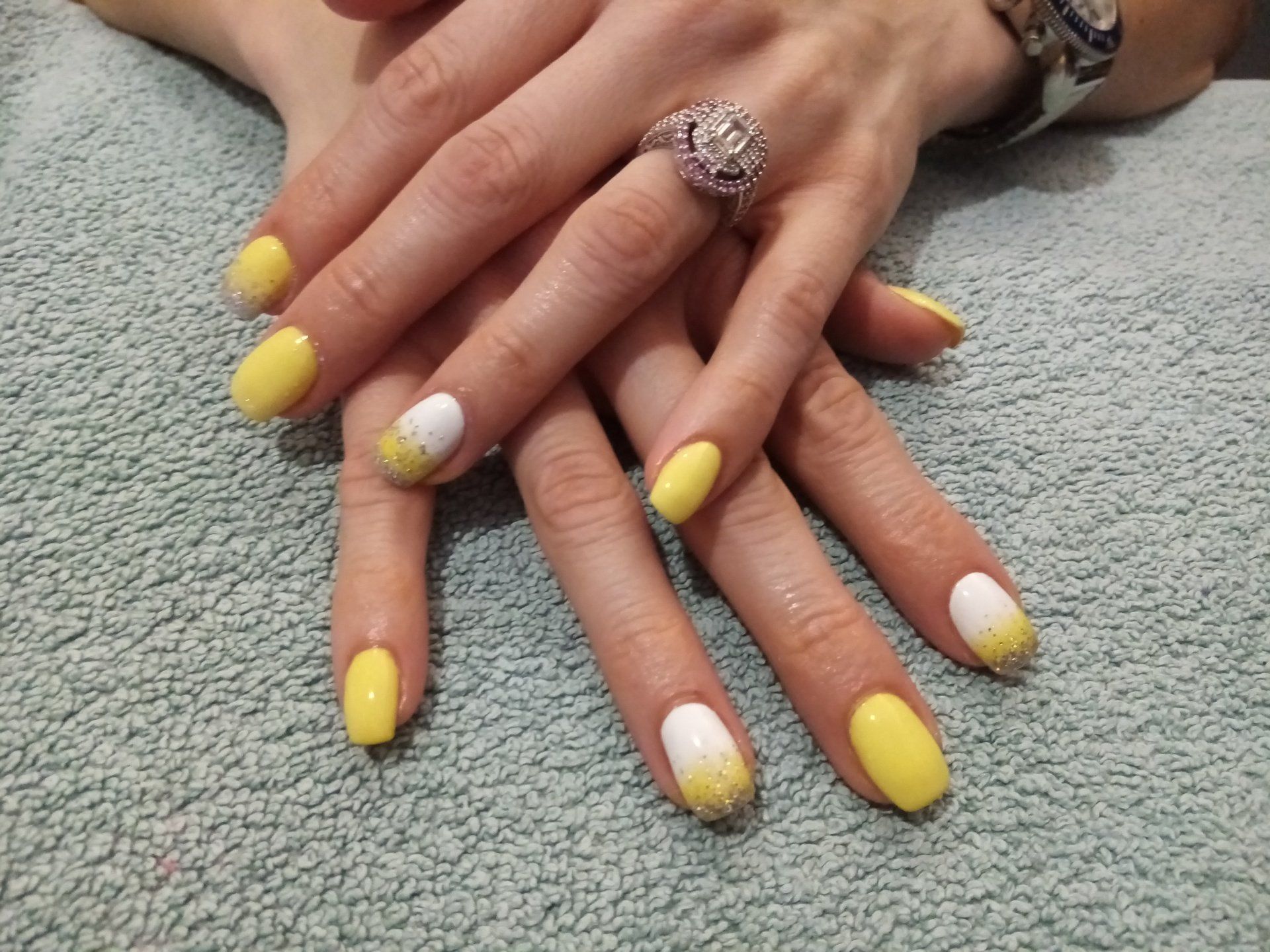 A woman 's hands with yellow and white nails and a ring on her finger