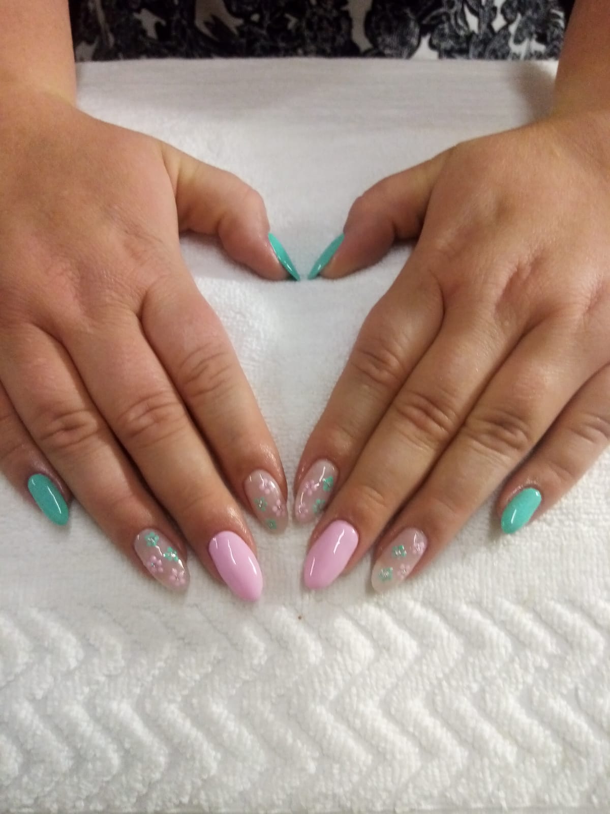A woman 's hands with pink and green nails on a white towel.