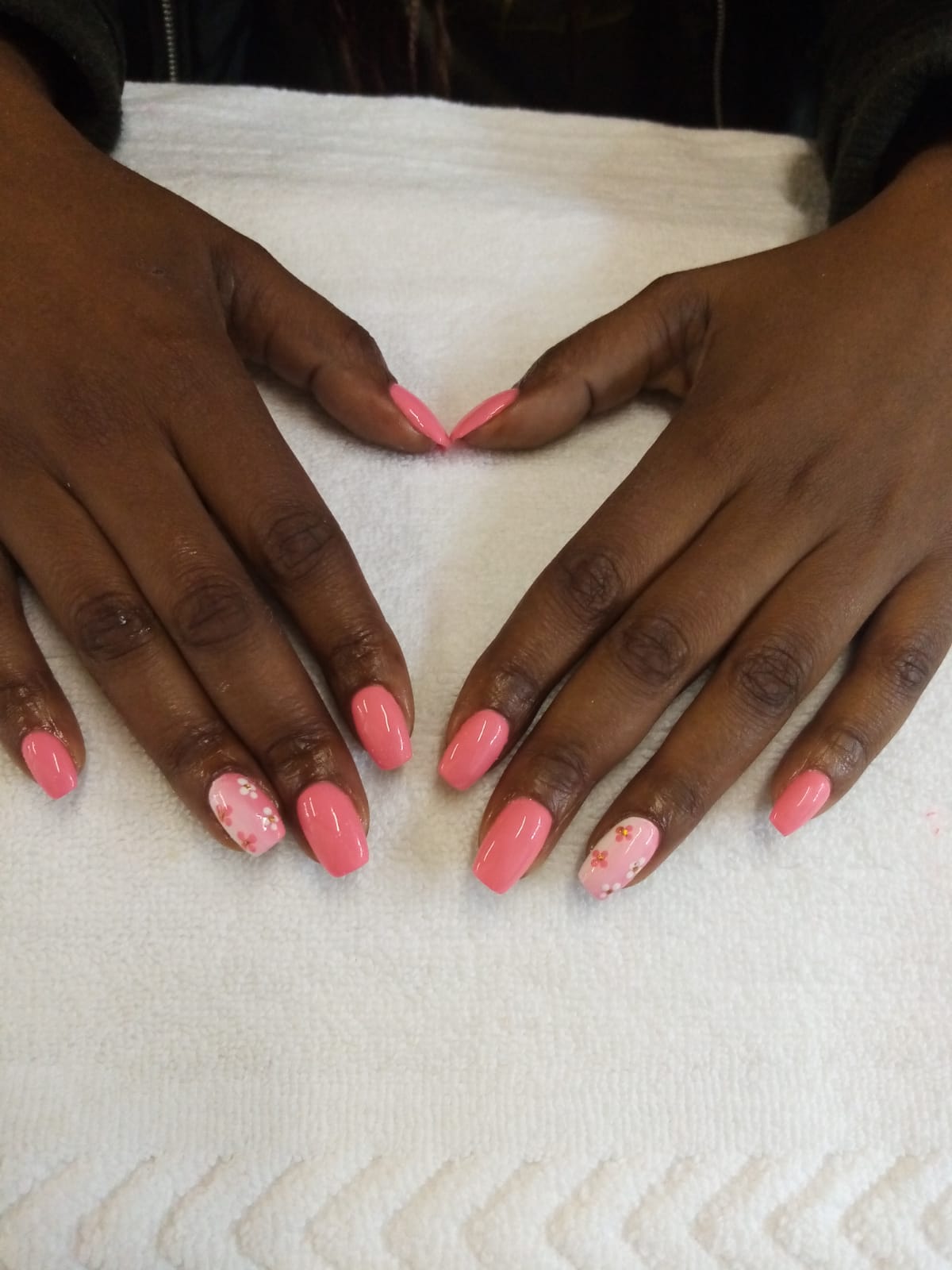 A woman with pink nails is making a heart shape with her hands