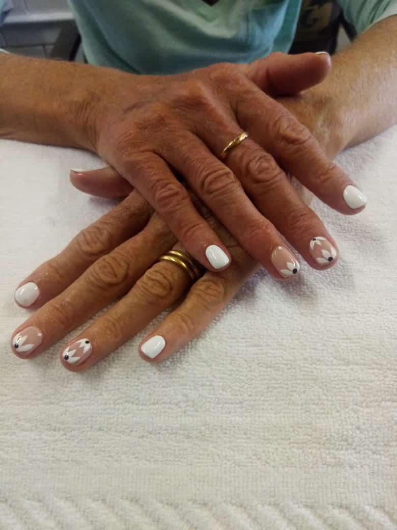 A close up of a person 's hands with white nails and gold rings.