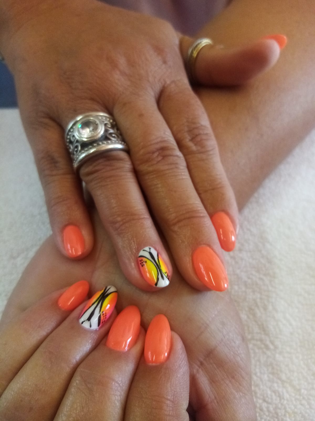 A woman 's hands with orange nails and a silver ring