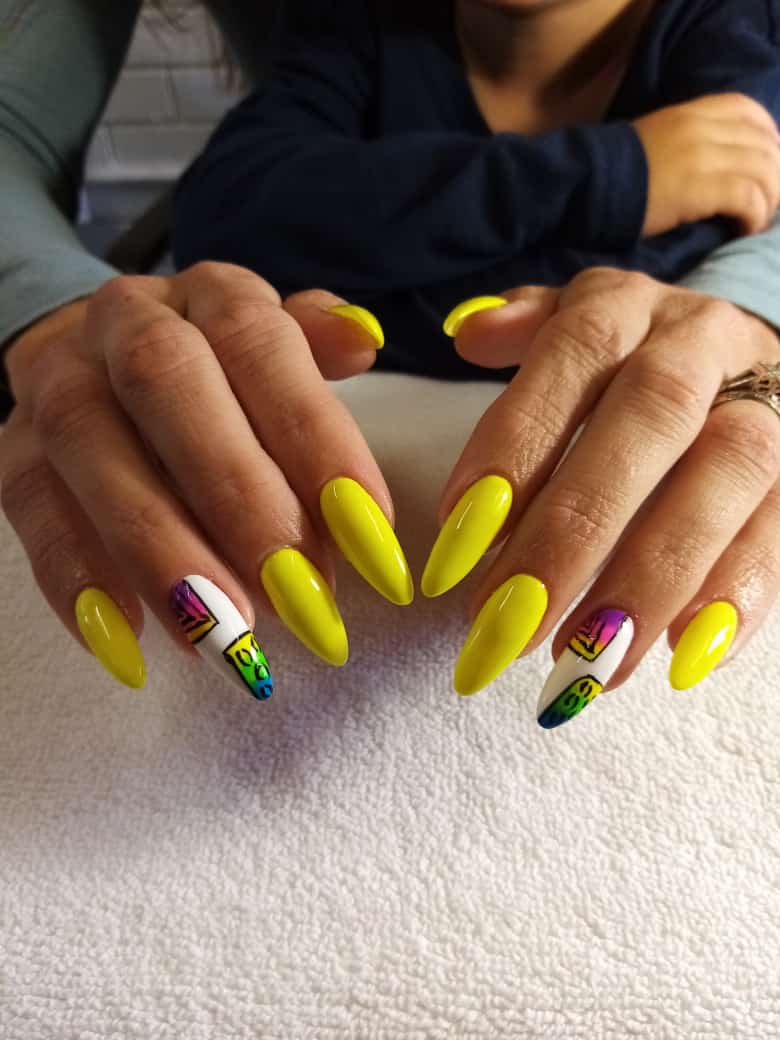 A woman 's nails are painted yellow with a rainbow design.