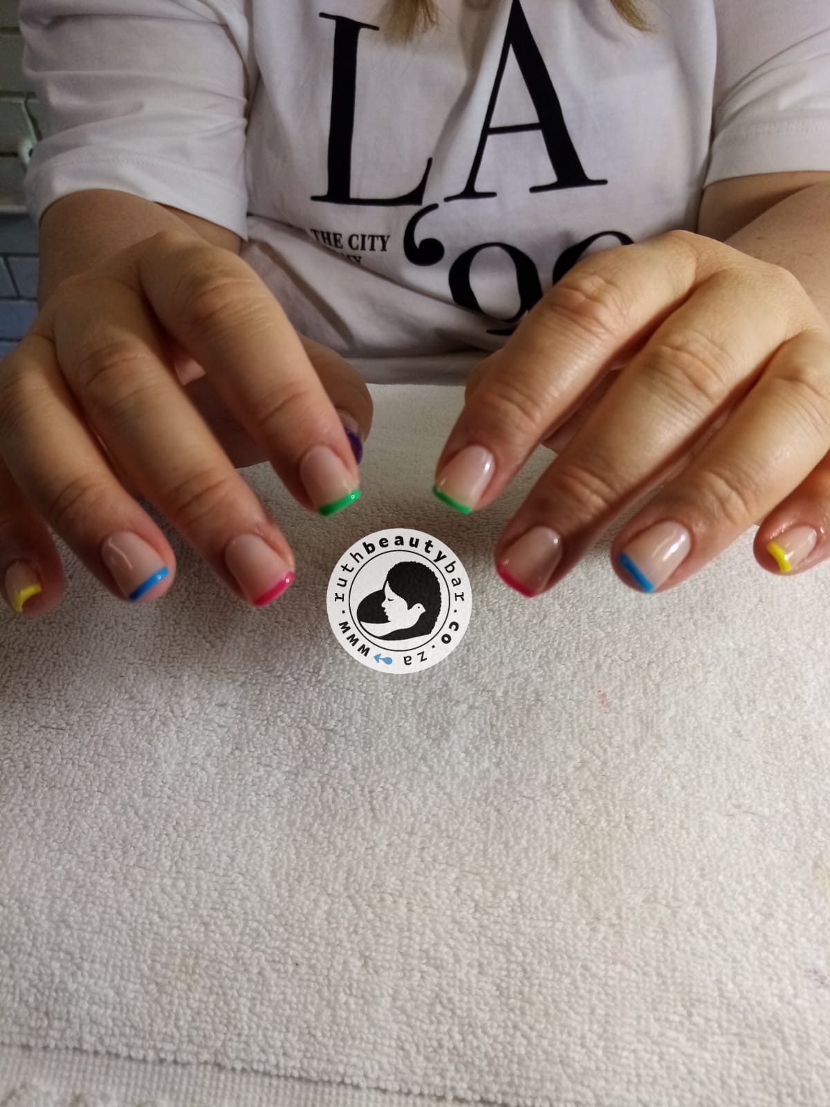A woman 's nails are painted in different colors and she is wearing a la shirt.