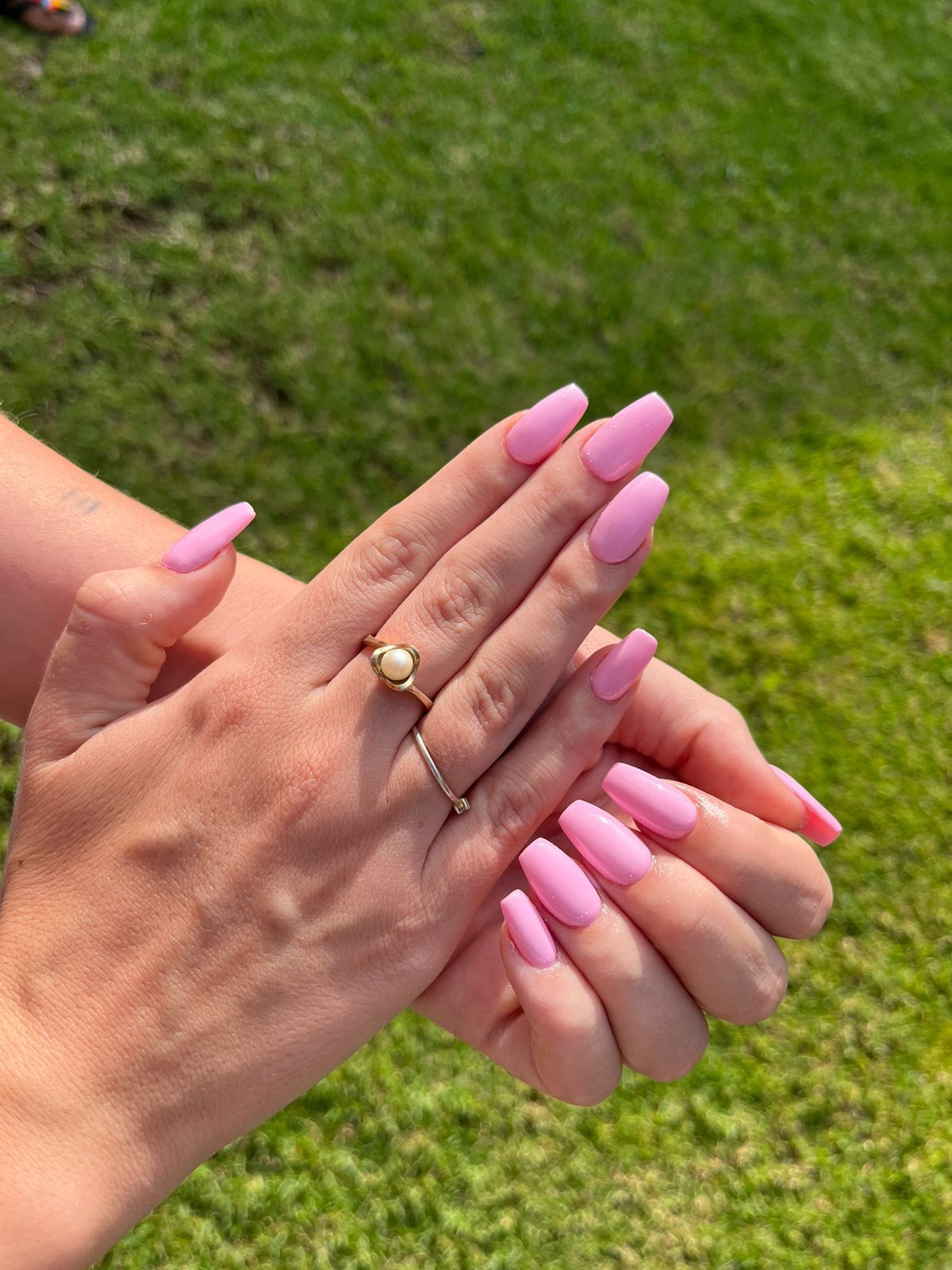 A close up of a woman 's hands with pink nails and a ring.