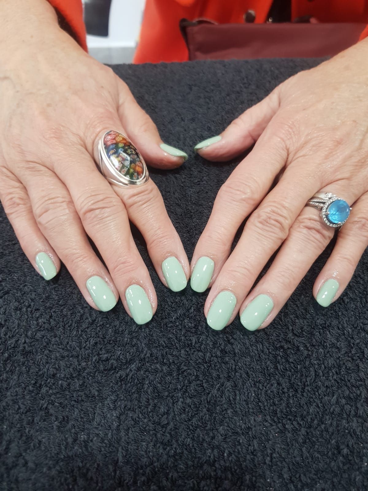 A woman 's hands with green nails and two rings on them